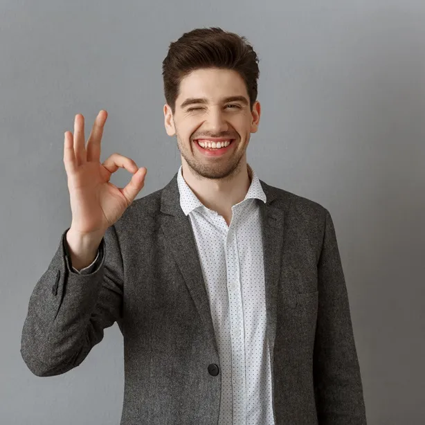 portrait of smiling businessman in suit showing ok sign against grey wall